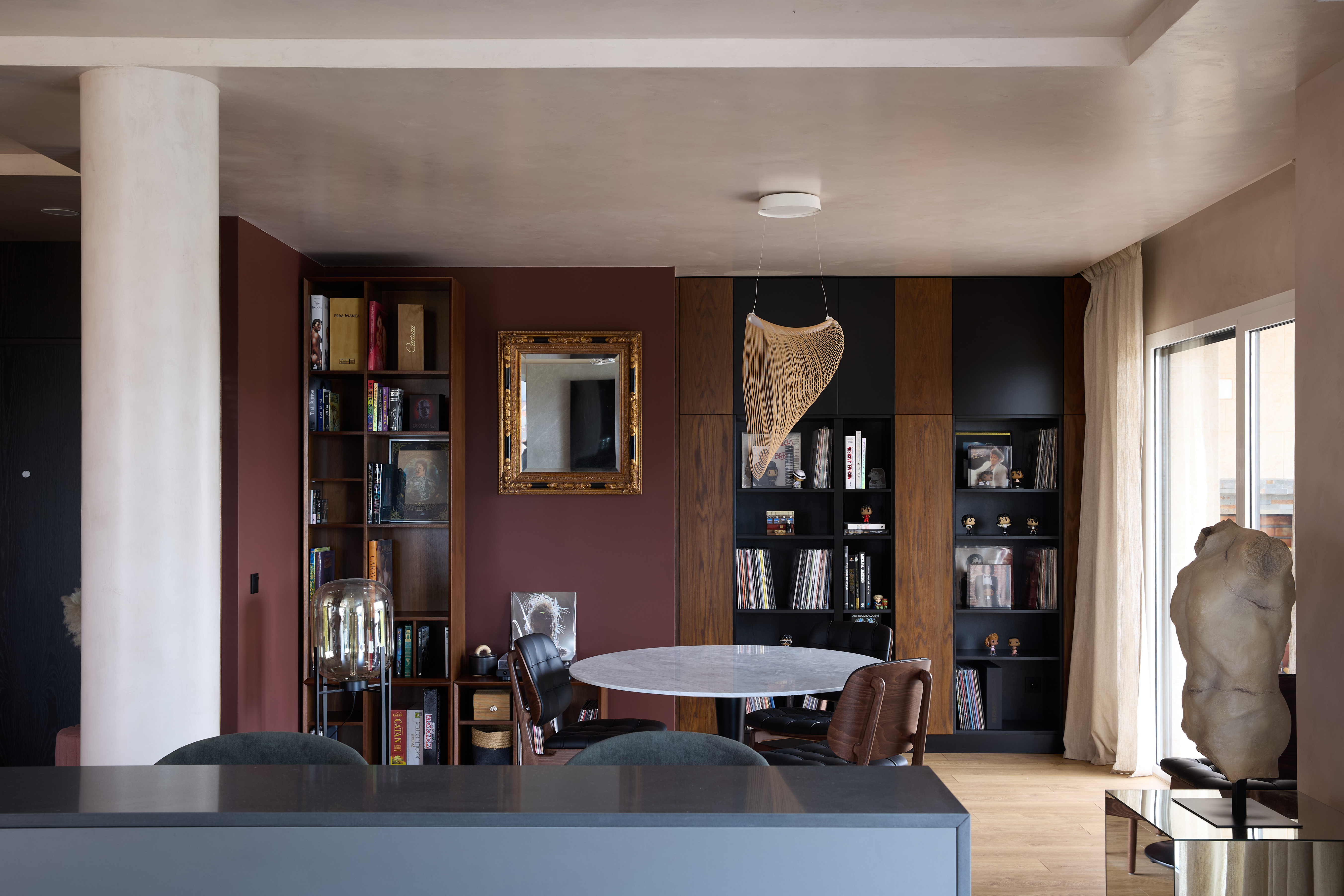 Collected living and dining interior with burgundy wall, bookshelves and sculptural object